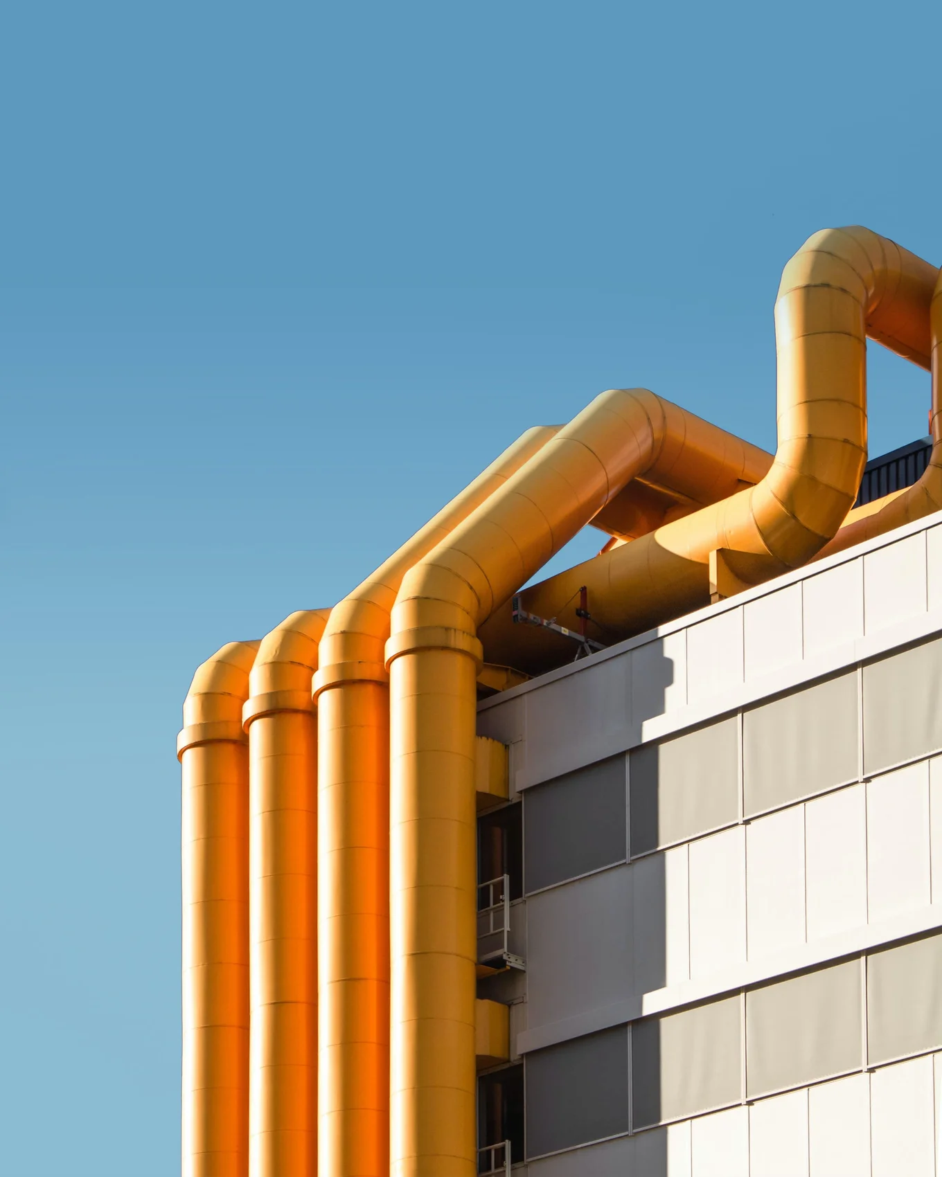 Yellow pipes on modern building against blue sky.