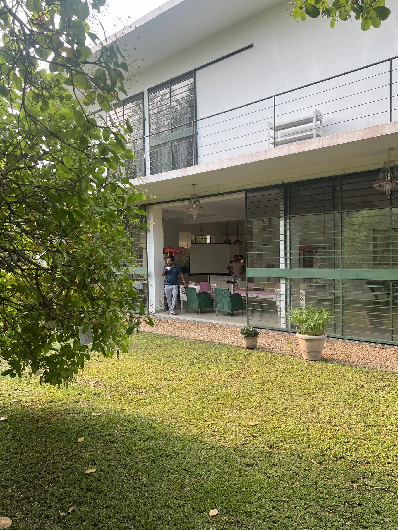 One of the participants stands in a big sliding doorway between the main house and the garden. He is drinking a cup of coffee and looking out over the lawn and trees.