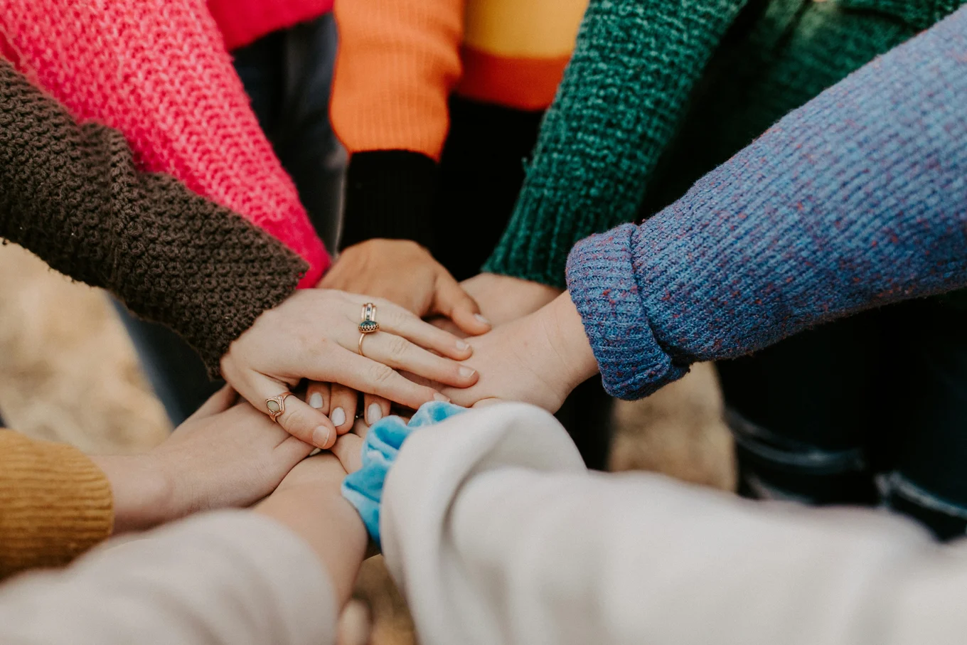 Hands stacked together, colorful sleeves visible.