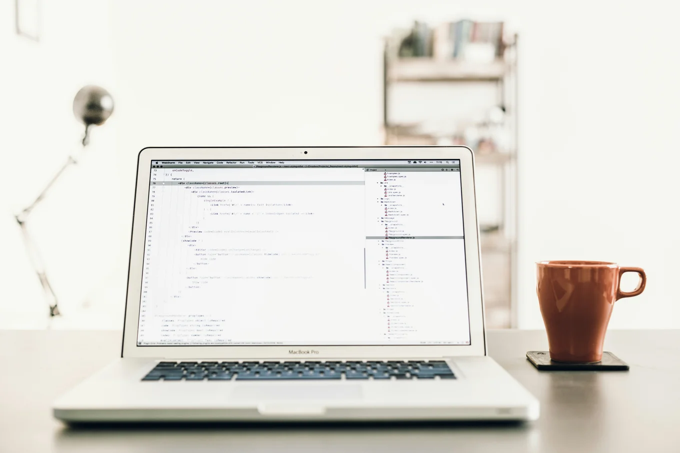 Laptop with code, orange mug, lamp, and shelf.