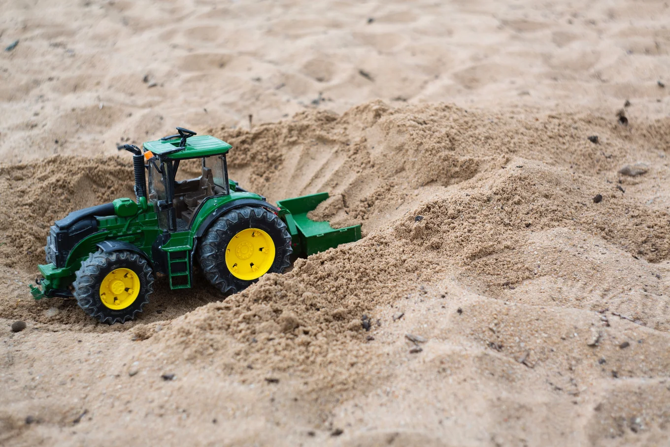 Toy green tractor on sand.