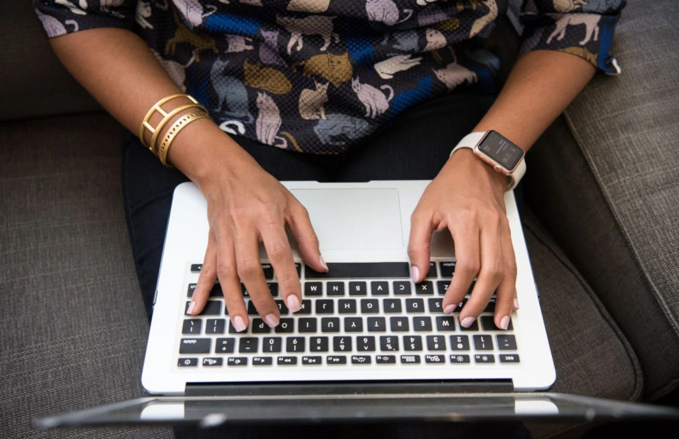 Hands typing on laptop; cat-print shirt, smartwatch.