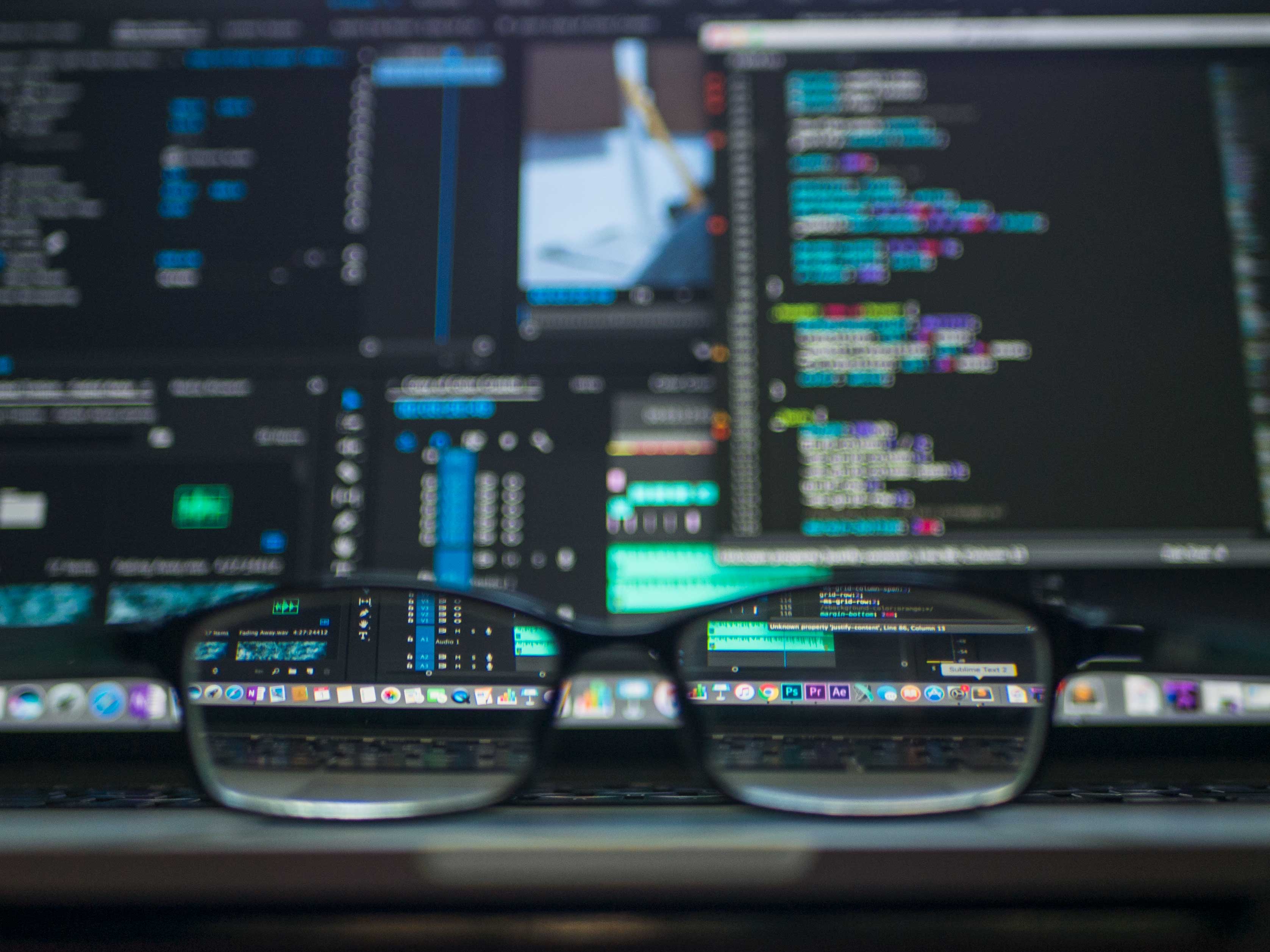 Glasses on keyboard, computer screen with code.