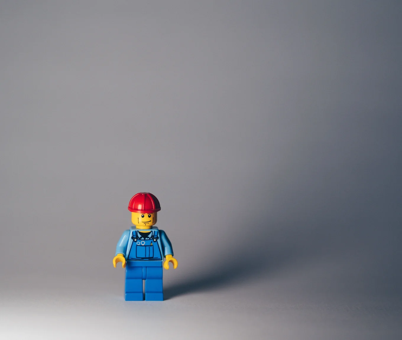 LEGO figure in blue outfit, red helmet, gray background.