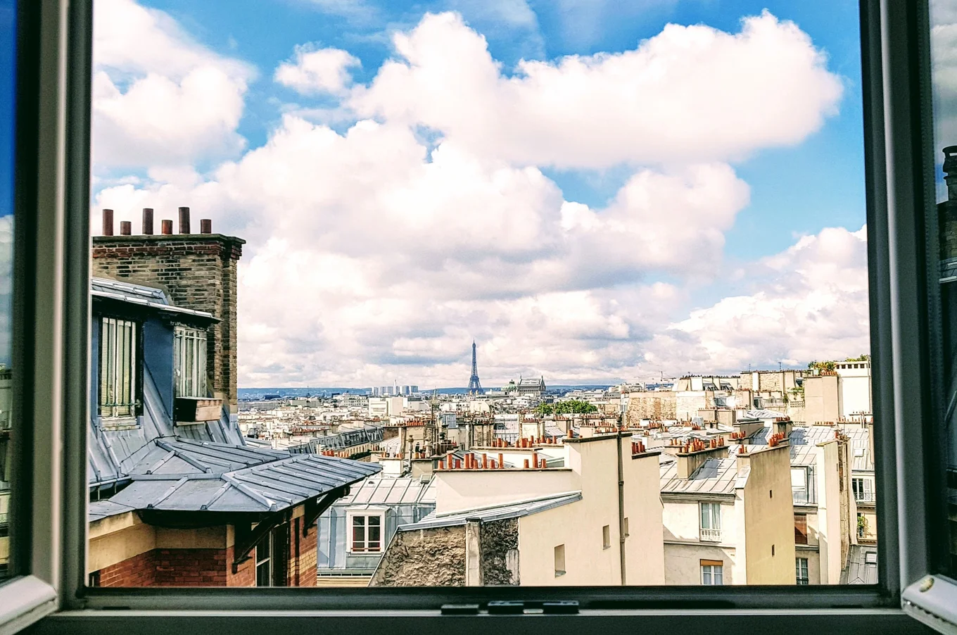 City rooftops, open window, cloudy sky, distant tower.