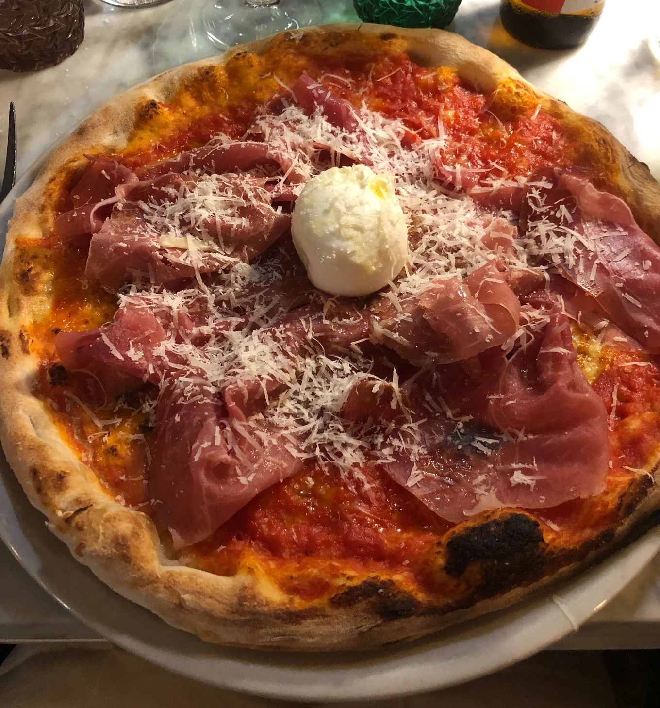 An Italian-style pizza with a whole piece of mozzarella cheese in the middle, surrounded by sliced meat.