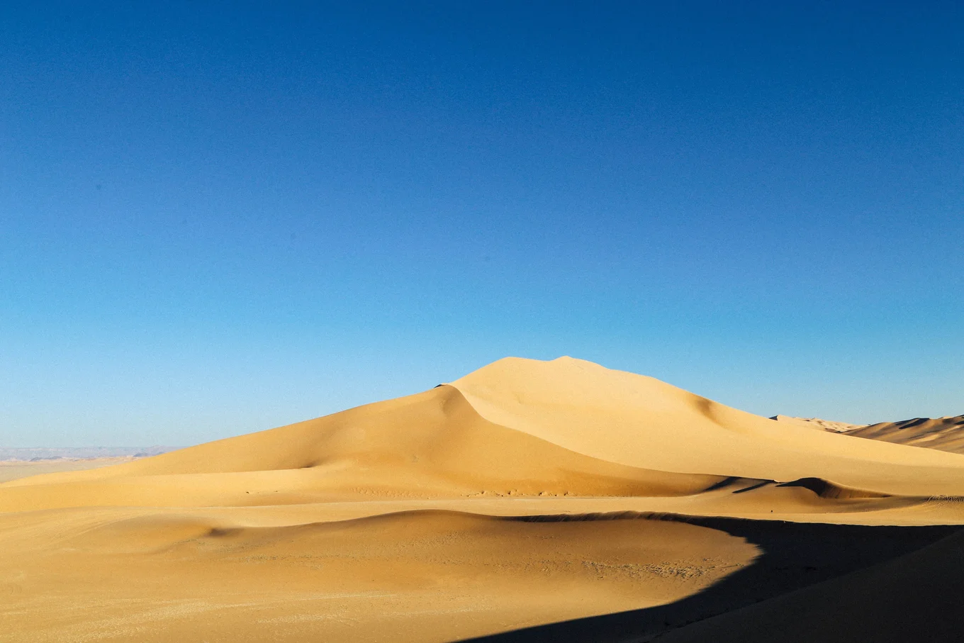 Yellow sand dunes under clear blue sky.