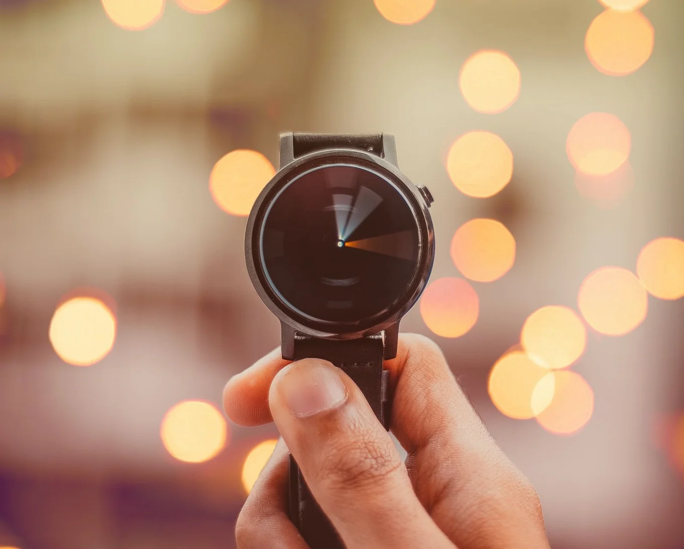 Hand holding black smartwatch, bokeh lights behind.